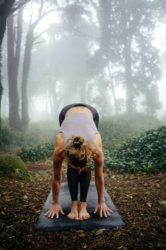 a woman is doing yoga in the woods on a foggy day with her hands behind her head