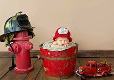 a baby wearing a fireman's hat sitting in a bucket next to a fire hydrant