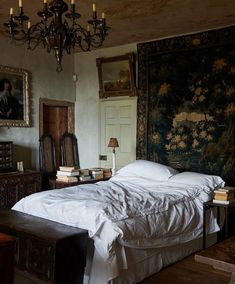 a bed sitting in a bedroom under a chandelier next to a painting on the wall