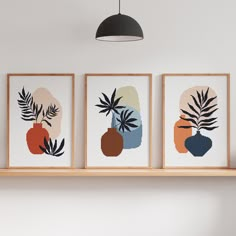 three framed art pieces hang on a wall above a shelf in a room with white walls