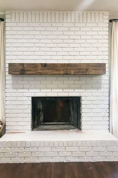 a white brick fireplace in a living room with wood flooring and curtains on the windows