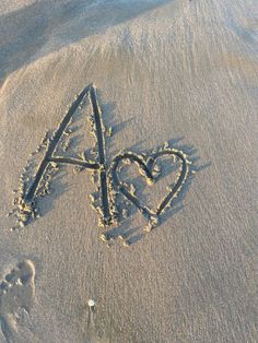 a heart and arrow drawn in the sand at the beach with an animal's paw