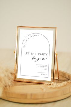 a sign that says let the party begin on top of a wooden tray with feathers