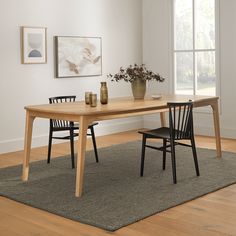 a dining room table with two chairs and a vase on the rug in front of it