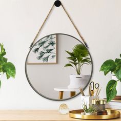 a round mirror hanging on the wall above a desk with office supplies and potted plants