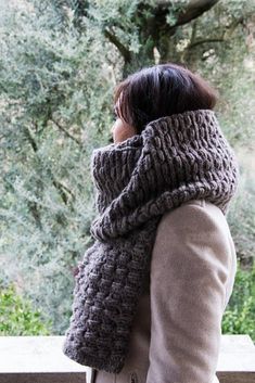 a woman standing in front of some trees wearing a knitted cowl neck scarf