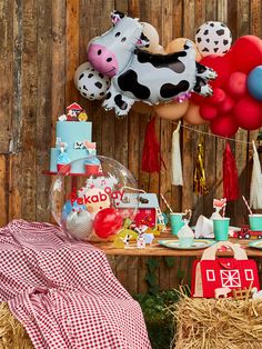 an outdoor birthday party with balloons, cake and farm animals on the fenced in area