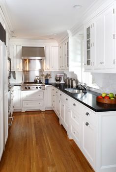 a kitchen with white cabinets and black counter tops, along with hardwood flooring in the middle