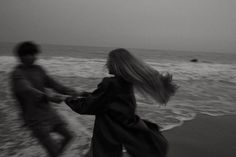 two people are running on the beach near the water and one is holding his hand