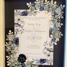 a blue and white wedding card in a frame with flowers on the front, along with a monogrammed design