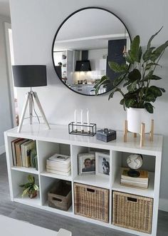 a white shelf with books, plants and pictures on it next to a round mirror