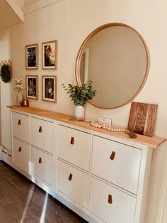 a white dresser topped with lots of drawers next to a wall filled with framed pictures