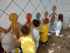 several children standing in front of a wall with paper cutouts on it and paint