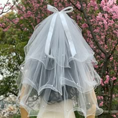 the back of a woman's head wearing a veil and dress with flowers in the background