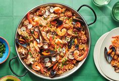 a pan filled with seafood and rice on top of a green table next to bowls of vegetables