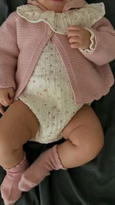 a baby is wearing a pink cardigan and matching socks while laying on a black blanket