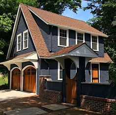 a blue house with brown shingles and two garage doors on the front door is surrounded by trees