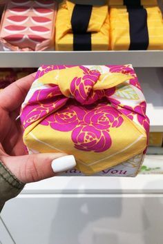 a hand holding a small yellow and pink gift box in front of some other boxes