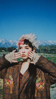 a woman with pink hair and gloves covering her face in front of the desert landscape