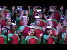 a group of children in red and green outfits with crowns on their heads are singing