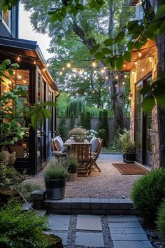 Cozy outdoor patio at dusk with string lights, wooden furniture, potted plants, trees, and a pathway of stepping stones, creating a serene ambiance. Quaint Backyard Ideas, Small Backyard For Entertaining, Hardscaping Backyard Ideas, Uneven Backyard Ideas, Small Backyard Landscaping On A Budget, Rowhouse Backyard, Small Backyard Ideas On A Budget, Small Garden Ideas On A Budget, Rental Backyard Ideas