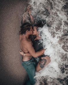 a man and woman laying on top of each other in the ocean with their arms around each other