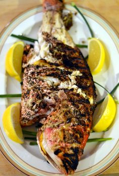 grilled fish on a plate with lemon wedges