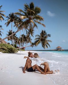 a man and woman are kissing on the beach with palm trees in the back ground