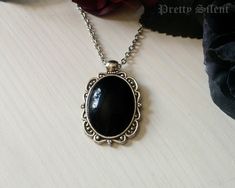 Handmade elegant, gothic style necklace  featuring a deep black glass cabochon that sits in a detailed antique silver ornate frame. Pendant size: 40 x 24 mm Cabochon size: 18 x 25 mm The necklace length can be chosen in the drop down menu.  Material: Antique silver plated metal alloy, glass cabochon All items come beautifully packaged. **PLEASE NOTE** : Standard Shipping is untracked to keep the shipping costs low. If you want to TRACK YOUR ORDER please select the SHIPPING UPGRADE at checkout! I Clubbing Shoes, Cabochon Necklace, Elegant Gothic, Black Jewel, Jewel Necklace, Ornate Frame, Gothic Style, Necklace Black, Deep Black