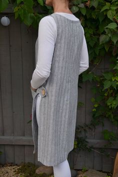 a woman standing in front of a fence wearing a gray vest and white tights