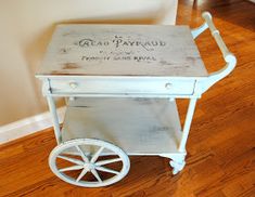 a white cart with wheels on the floor in front of a wall and hardwood floors