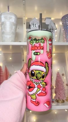 someone holding up a pink christmas themed tumbler in front of shelves with other holiday decorations