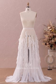 a white wedding dress with ruffles on the bottom and side, in front of a