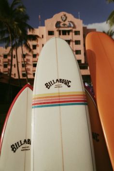 three surfboards are stacked on top of each other in front of a building and palm trees