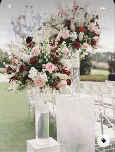 two tall vases filled with flowers sitting on top of a grass covered field next to white chairs