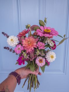 a person holding a bouquet of flowers in front of a blue door with white and pink flowers