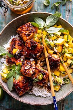 a bowl filled with rice and chicken next to chopsticks on top of it