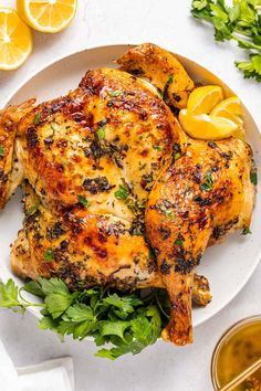 a white plate topped with chicken next to lemon wedges and garnished with parsley