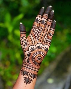 a woman's hand with henna on it and green leaves in the background