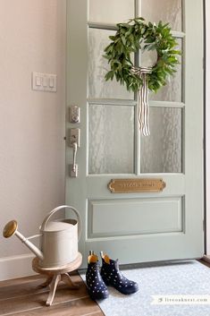 a green door with a wreath on it next to two rubber boots and a watering can