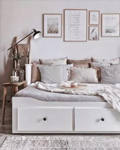 a white bed with lots of pillows on top of it and pictures above the headboard