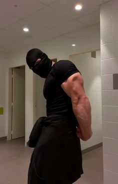 a man in a black shirt and mask is standing in a room with white walls