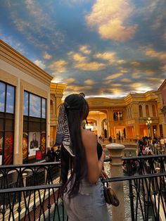 a woman is standing on a balcony looking up at the clouds in the sky above her