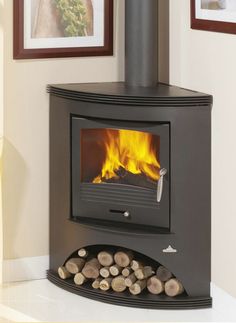 a wood burning stove with logs in the foreground and pictures on the wall behind it