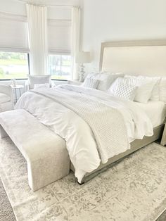 a large white bed sitting in a bedroom next to a window with curtains on the windowsill