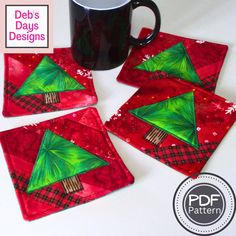 four red coasters with green christmas trees on them and a black coffee mug in the middle