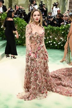 a woman in a long dress standing on a green carpet with people taking pictures behind her