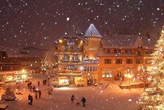 people are walking through the snow in front of a building with christmas lights on it