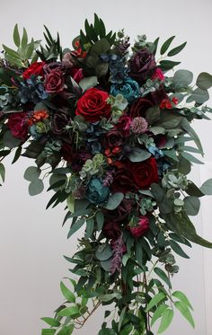 a large bouquet of flowers and greenery on a table in front of a white wall