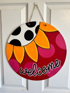 a welcome sign hanging on a door with polka dots and sunflowers painted on it